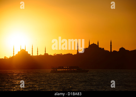 Goldener Sonnenuntergang über blaue Moschee mit Hagia Sophia in der Silhouette am Bosporus mit Boot Istanbul Türkei Stockfoto