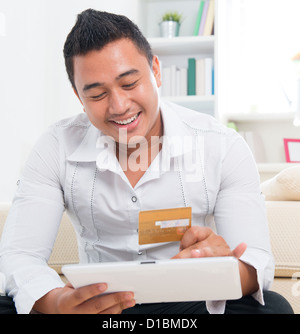 Südostasiatische Mann online-shopping, Hände halten, Kreditkarte und Registerkarte "Computer" zu Hause sitzen. Stockfoto