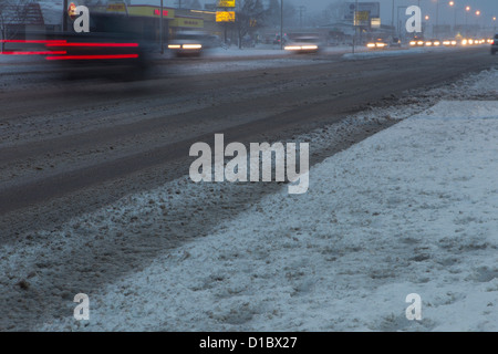 Schwanz und Scheinwerfer zu verwischen, als am frühen Morgen, den Verkehr durch Schnee schuftet und slush auf einer Stadt-Straße. Stockfoto