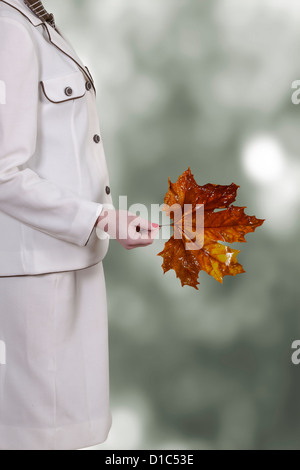 eine Frau in einem weißen Rock Anzug hält eine herbstliche rote Blatt aus einer Platane Stockfoto