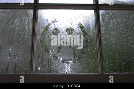 Trauriges Gesicht im Fenster Kondensation gezeichnet. Stockfoto
