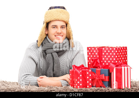 Ein lächelnder Mann mit Hut und Krawatte liegen auf einem Teppich in der Nähe von Geschenken auf weißen Hintergrund isoliert Stockfoto