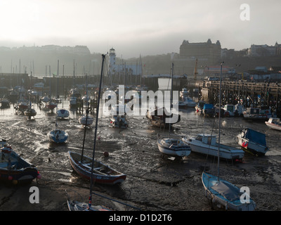 Sportboote auf dem Schlamm bei Ebbe im Hafen von Scarborough North Yorkshire UK an einem nebligen Winternachmittag Stockfoto