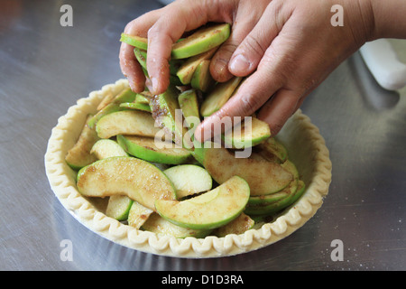 Eine Nahaufnahme von einer Frau einen Tortenboden mit Apfelscheiben zu füllen. Stockfoto