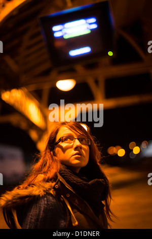 Eine junge Frau Teenager-Mädchen allein auf einem verlassenen Bahnhof Bahnsteig warten auf einen Zug in der Nacht, UK Stockfoto