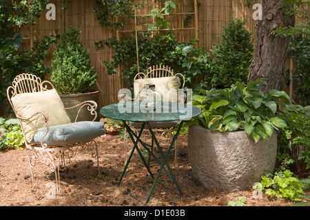 Tannennadeln Gärten schaffen eine Terrasse für ein Sitzmöbel Bereich Metall-Stühle und Tisch große Betonbehälter mit Hosta gefüllt Stockfoto