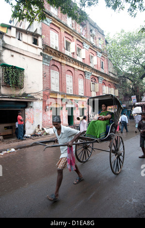 Frau Reiten im laufenden Rikscha, vorbei an wunderschönen alten Raj Ära Kolkata Gebäude in Kolkata Backstreet, West Bengalen, Indien, Asien Stockfoto