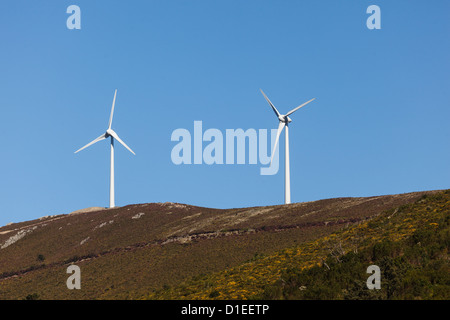 2 Windmühlenturbinen zur Stromerzeugung auf einem Hügel im Hintergrund mit blauem Himmel Stockfoto