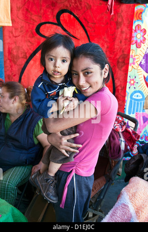 schönen lächelnden jungen mexikanisches Mädchen hält ihr Baby Bruder hat einen unordentlichen Mund durch den Verzehr von Bananen-Oaxaca de Juárez-Mexiko Stockfoto