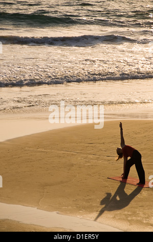 Vertikale Porträt einer Dame praktizieren Yoga am Strand bei Sonnenuntergang in Varkala, Kerala. Stockfoto