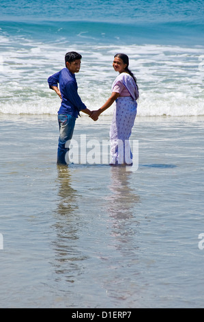 Vertikale Porträt eines jungen indischen Brautpaar stehenden im Meer bekleidet voll Hand in Hand am Strand von Varkala, Kerala Stockfoto
