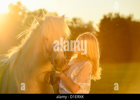 Lächelnde Frau in weißem Kleid mit Pferd auf der Wiese Stockfoto