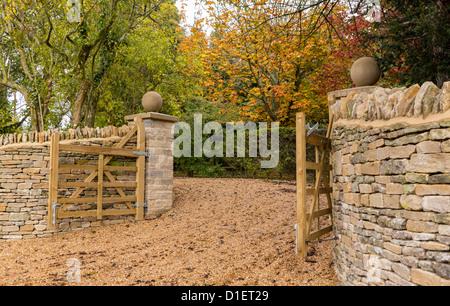 Stilvolle Holztore über Kies fahren und Cotswold Steinmauer Stockfoto