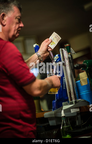 Ein Barkeeper einen Pint kaltes Lager ziehen und halten eine Anmerkung £10 an einem Samstagabend in einem Working Mens Club, UK Stockfoto