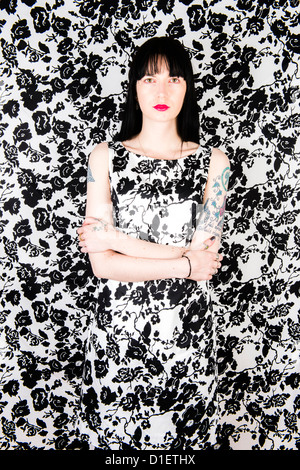 Eine dunkelhaarige Frau trägt eine schwarzen und weißen Kleid stand vor einem passenden gemusterten Hintergrund Stockfoto