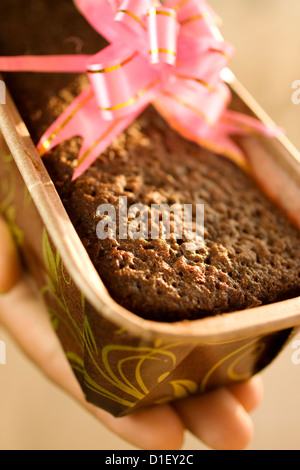 Detail einer Pflaume Weihnachtskuchen statt mit der hand. Die Sonne scheint auf dem Kuchen in einem rosa Geschenkband umwickelt. Ein frisch gebackenes Weihnachtsgeschenk. Stockfoto