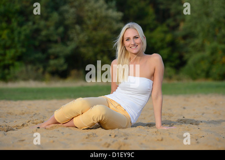 Glückliche junge, blonde Frau am Sandstrand Stockfoto