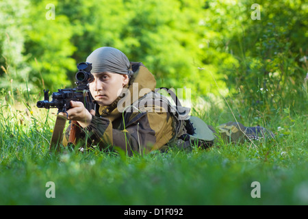 Soldat in Camouflage mit einer Kalaschnikow auf der Wiese liegend Stockfoto