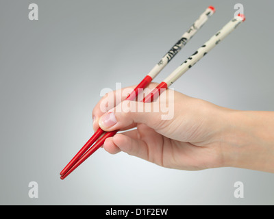 Nahaufnahme von weiblicher Hand mit Stäbchen auf grauem Farbverlauf Hintergrund Stockfoto