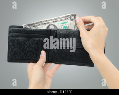 weibliche Hände halten eine schwarze Leder-Portemonnaie zerbröckelte Geld entziehen, auf grauem Farbverlauf Hintergrund Stockfoto