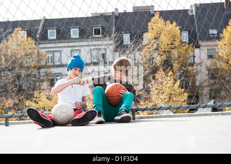 Zwei Jungs sitzen am Sportplatz mit Kugeln Stockfoto