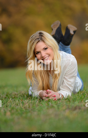 Lächelnde blonde junge Frau, die im herbstlichen Wiese liegend Stockfoto