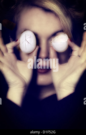 eine Frau hält zwei gebrochenen Eiern vor ihren Augen Stockfoto