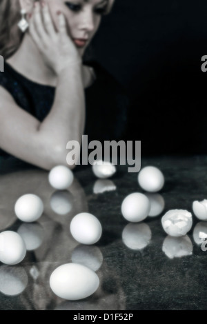 eine Frau sitzt an einem Tisch vor mehrere Eizellen, einige von ihnen gebrochen Stockfoto