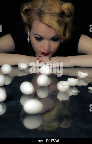 eine Frau sitzt an einem Tisch vor mehrere Eizellen, einige von ihnen gebrochen Stockfoto