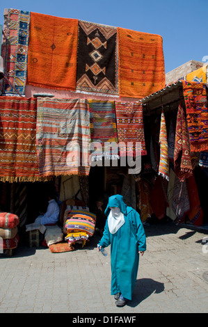 Eine Frau in islamischer Kleidung vorbei an Teppiche hängen rund um einen Eingang zum Souk in Marrakesch, Marokko, Nordafrika Stockfoto