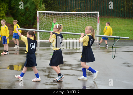 Schülerinnen und Schüler tragen ein Korbball-Ziel in unserer lieben Frau & St. Werburgh's katholische Grundschule in Newcastle-under-Lyme, Staffordshi Stockfoto