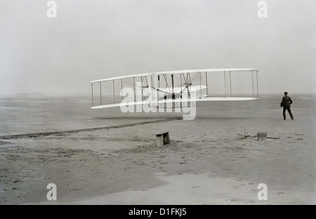 Ersten erfolgreichen Flug der Wright Flyer der Gebrüder Wright. Die Maschine reiste 120 ft in 12 Sekunden bei 10:35 in Kitty Hawk, North Carolina. Orville Wright wurde an der Steuerung der Maschine, Bauchlage auf der unteren Tragfläche mit den Hüften in die Wiege, die den Flügel-verwerfen Mechanismus betrieben. Wilbur Wright lief neben die Maschine auszugleichen, und hat soeben seinen Einfluss auf die vorwärts aufrechte des rechten Flügels auf dem Foto. Der Start Schiene, Flügel-Rest, eine Spule-Box und andere Gegenstände benötigt zur Flugvorbereitung sind sichtbar hinter der Maschine. Dies war die erste Sust betrachtet. Stockfoto