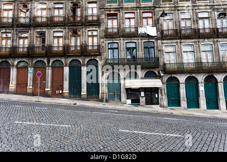 Fassade der unteren Etagen eines Mehrfamilienhauses auf einem steil abfallenden Straße mit Kopfsteinpflaster in Porto portgal. Stockfoto