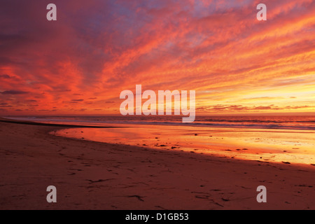 Nach Sonnenuntergang leuchtet der Himmel. Es spiegelt die leuchtenden Farben auf dem Ozean, bewölktem Himmel und auf dem Sand in Carlsbad, CA Stockfoto