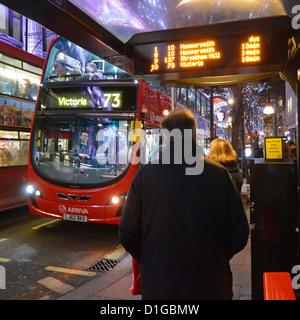 Straßenszene London West End roten Doppeldecker Bus Fahrer Passagiere warten an der Bushaltestelle Unterschlupf bei Nacht Ankunftszeiten auf elektronische Anzeige Stockfoto