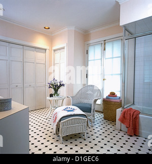 Badezimmer weißen geflochtenen Chair und Ottoman mit blau grau, weiße Kissen Quilt über osmanische großen weißen lackierten Schrank auf hängt Stockfoto