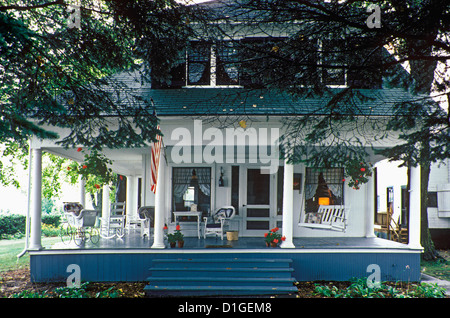 AUßEN ziemlich Ferienhaus mit großer Veranda mit Säulen Veranda rund um Dormer Windows amerikanische Flagge Wicker nach Hause Stockfoto