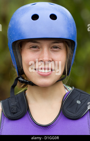 Ein Nahaufnahme-Porträt einer Frau, die einen blauen Schutzhelm mit Belüftungslöchern und eine lila gepolsterte Weste mit schwarzen Schulterprotektoren trägt. Sie lächelt direkt in die Kamera, mit ihrem Licht Stockfoto