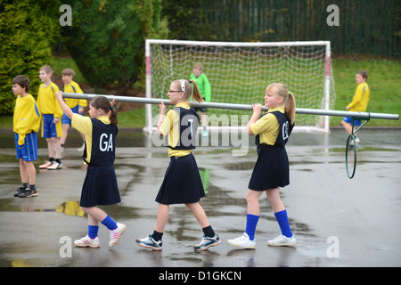 Schülerinnen und Schüler tragen ein Korbball-Ziel in unserer lieben Frau & St. Werburgh's katholische Grundschule in Newcastle-under-Lyme, Staffordshi Stockfoto