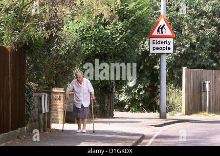 Ältere Dame gehen mit zwei Stöcken vorbei an einem Senioren-Schild. Stockfoto