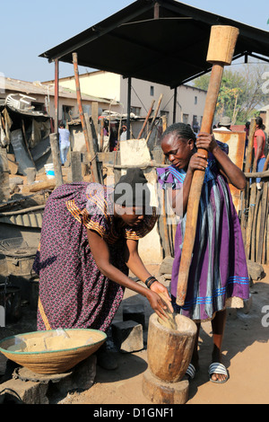 Zwei Frauen stampfen Hirse (Sorgum) mit Mörser und Pestel. Camp in einer schlechten Nachbarschaft von Tsumeb, Namibia Stockfoto