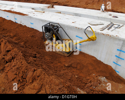 vibrierende Platte kompakter Verfüllung neben einem Streifenfundament der großen Brücke auf neue Straße Bau Website uk Stockfoto