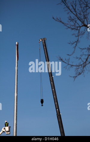 Mann im Eimer Aufzug neben Stahl Strommast mit Kranausleger. Stockfoto