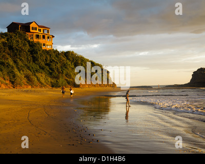 Zwei männliche Surfer Fuß am Strand Surfbretter zu tragen, während eine Person im Wasser in Nicaragua bei Ebbe steht Stockfoto