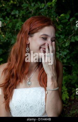 Rothaarige Frau außerhalb in einem Feld trägt ein Hochzeitskleid, mit der Hand über den Mund lachen Stockfoto