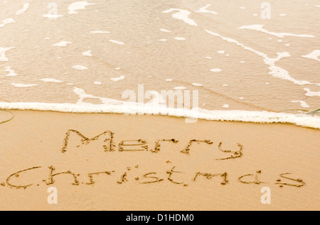 Frohe Weihnachten-Zeichen im Sand am Strand mit Wellen nähert sich geschrieben Stockfoto