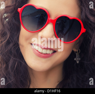 Schöne junge Frau mit freundlich einladende Lächeln herzförmige Sonnenbrille Stockfoto