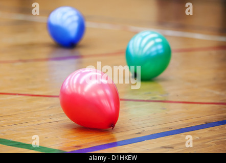 Drei bunte Luftballons auf Holzboden Sporthalle. Konzept der RGB-Farbschema Stockfoto