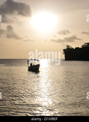 Kleines Boot verankert in einem silbernen Meer unter einer goldenen Himmel weiße Kugel untergehenden Sonne, Nordende Morne Rouge Strand, Grenada, West Indies Stockfoto