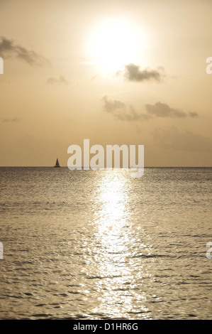 Horizon Yacht Segeln über eine Silber-graue Meer unter einer goldenen Himmel weiße Kugel untergehenden Sonne, Morne Rouge Strand, Grenada, West Indies Stockfoto